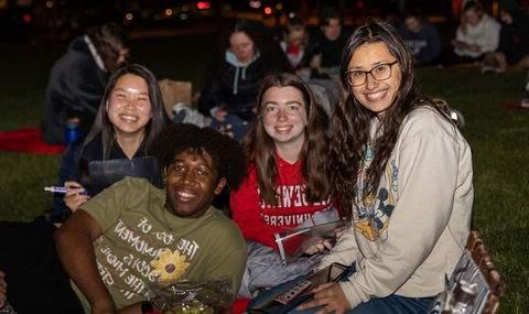 Four students smiling together, outside on the Boyden Quad, playing giant bingo